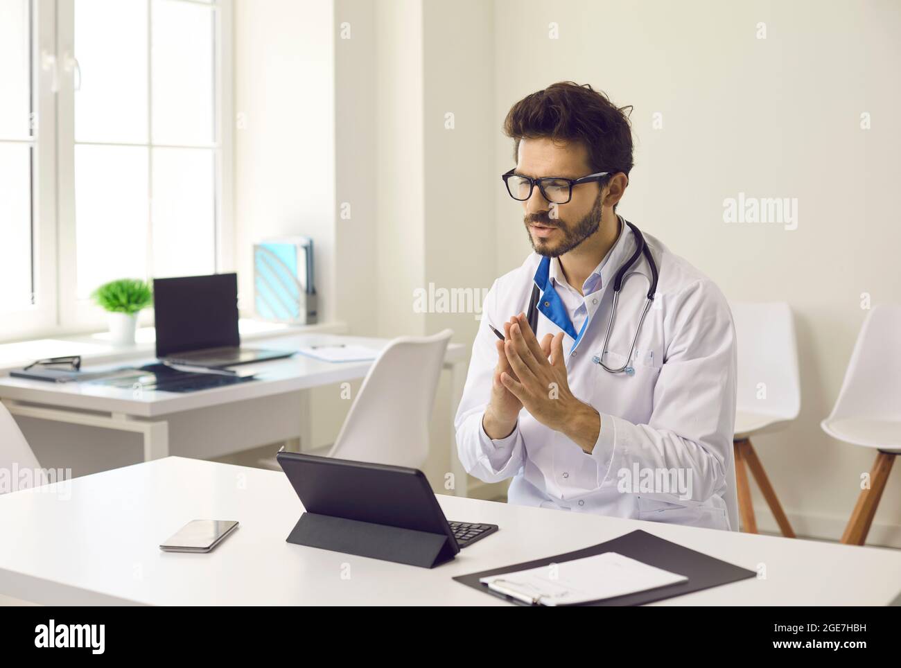 Médecin assis au bureau avec une tablette et parlant au patient lors d'un appel vidéo Banque D'Images