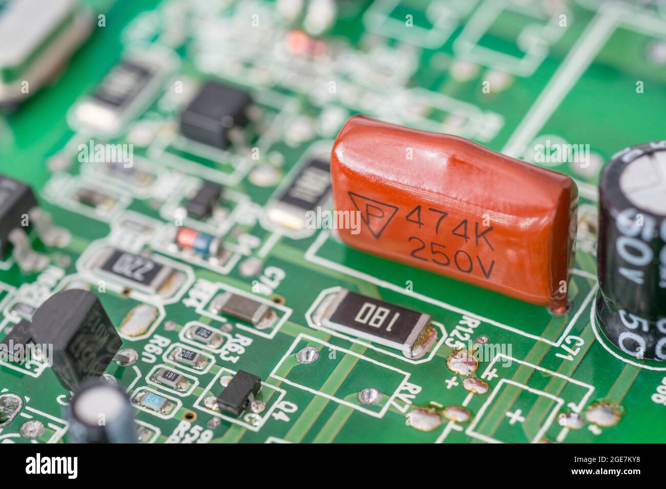 Gros plan du condensateur à film polyester trempé de couleur orange sur la carte de circuit imprimé verte. Pour condensateur au plomb, petits composants électroniques. Fabricant non identifié Banque D'Images