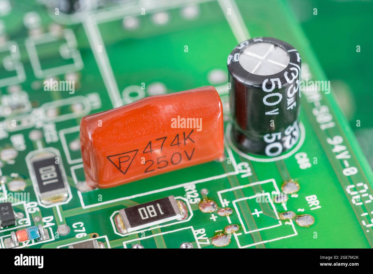 Gros plan du condensateur à film polyester trempé de couleur orange sur la carte de circuit imprimé verte. Pour condensateur au plomb, petits composants électroniques. Fabricant non identifié Banque D'Images