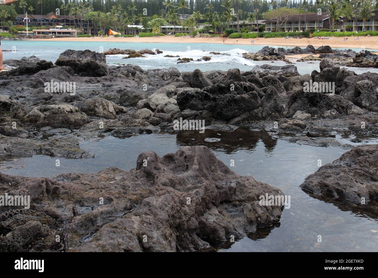 Des bassins de marée se sont formés sur des roches volcaniques bordant la plage de sable des touristes de la baie de Napili sur la plage et dans l'eau à Maui, Hawaï Banque D'Images