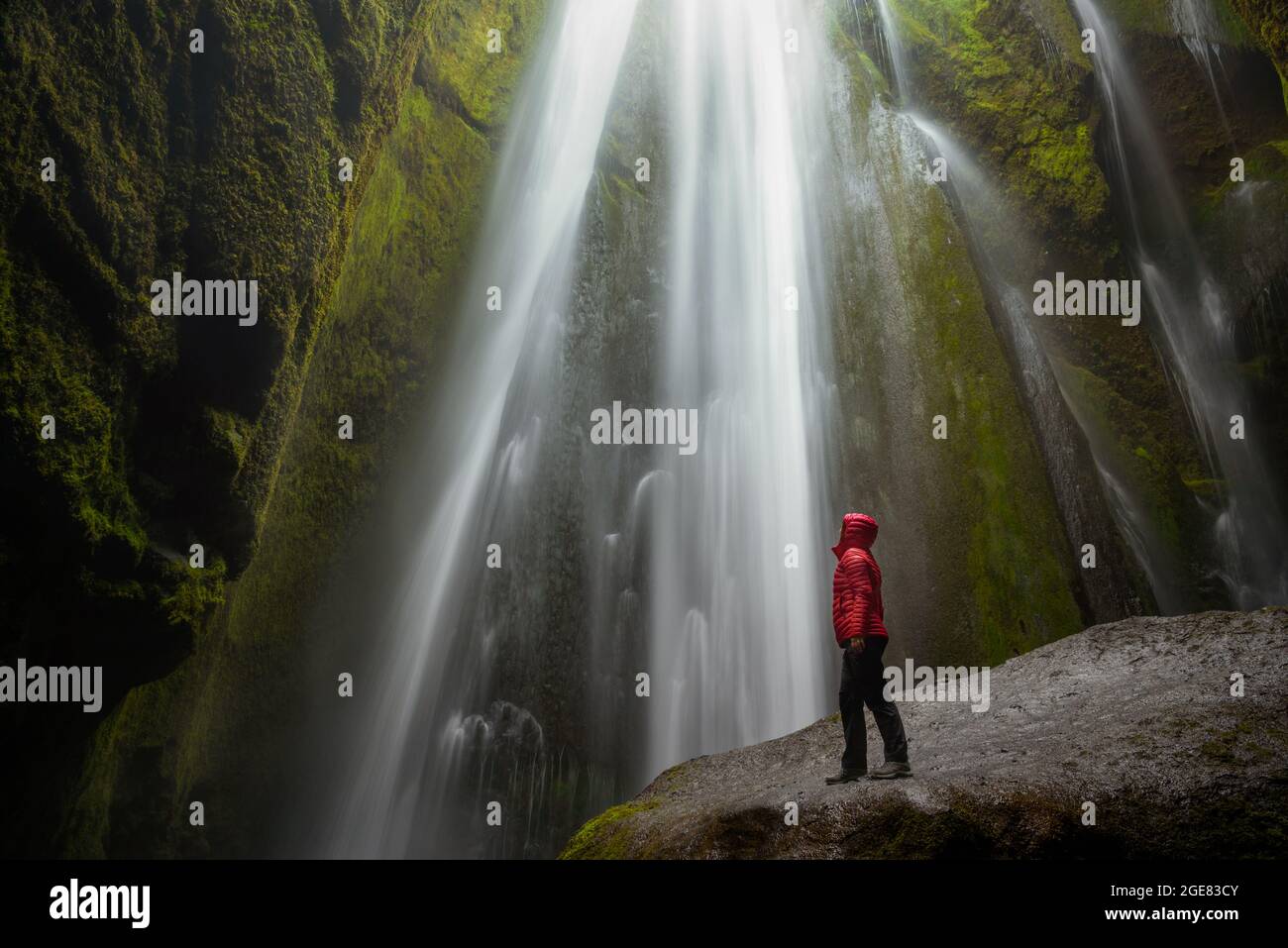 Femme sur un rocher mouillé au pied d'une cascade majestueuse dans un étroit canyon Banque D'Images
