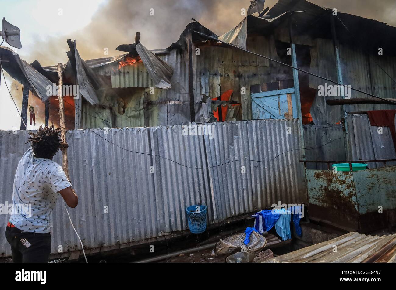 Nairobi, Kenya. 17 août 2021. Un résident utilise une bûche de bois pour empêcher le feu de se propager à Bombolulu, Kibera.les résidents se sont joints aux mains pour aider à mettre un feu qui s'est produit aujourd'hui après-midi à partir de fils électriques enchevêtrés fournissant l'alimentation à différentes maisons. Le feu a rasé douze maisons et propriétés laissant la plupart des résidents bloqués. Crédit : SOPA Images Limited/Alamy Live News Banque D'Images
