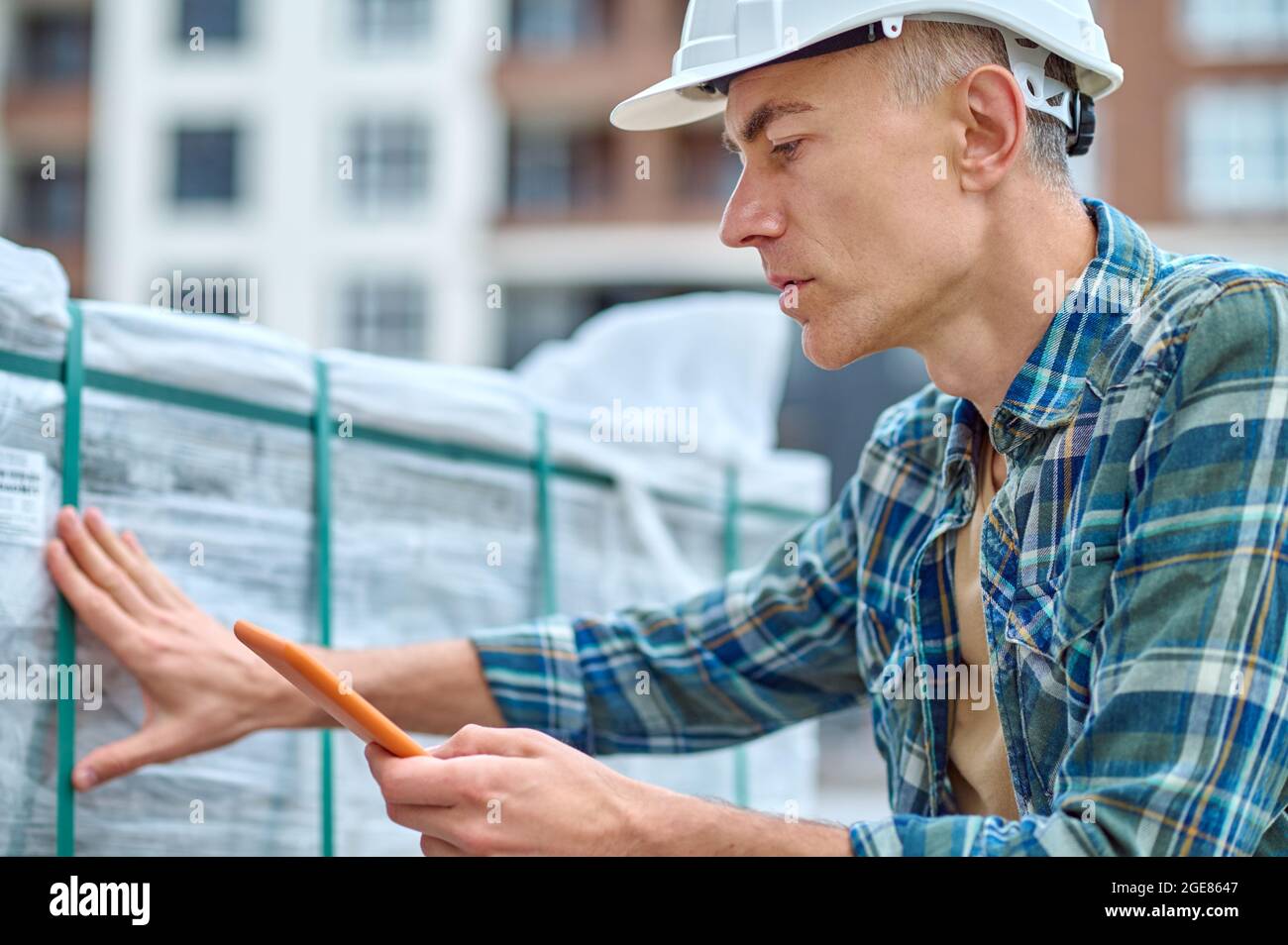 Travailleur sérieux dans un casque de chantier touchant les matériaux de construction Banque D'Images