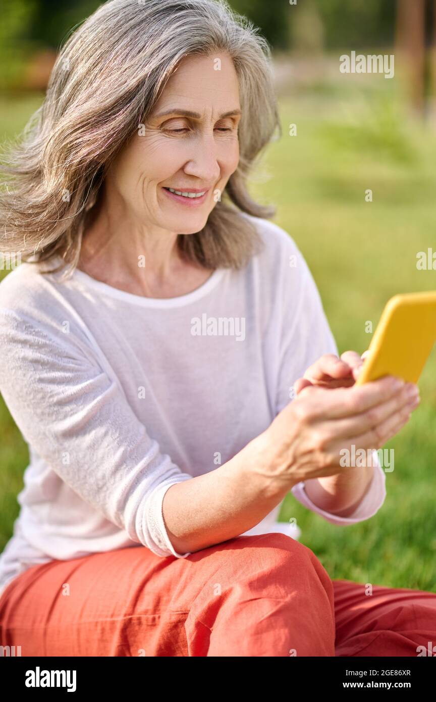 Femme adulte dans des vêtements décontractés avec un smartphone à l'extérieur Banque D'Images