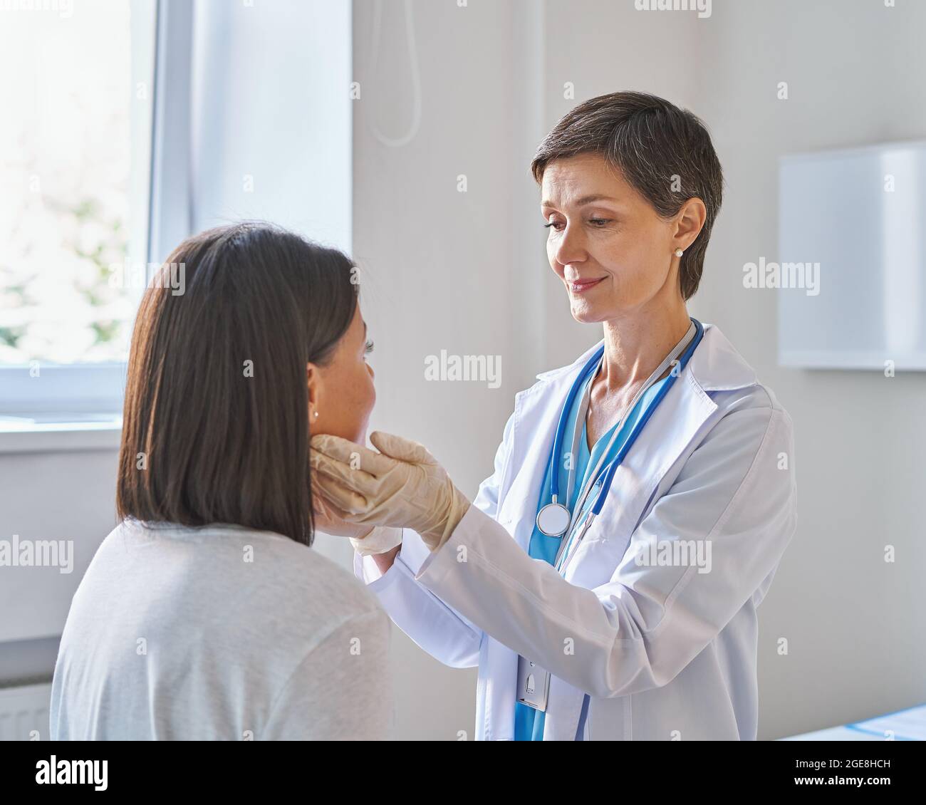 Femme d'âge moyen médecin portant des gants pour vérifier les maux de gorge ou les glandes thyroïdiennes Banque D'Images