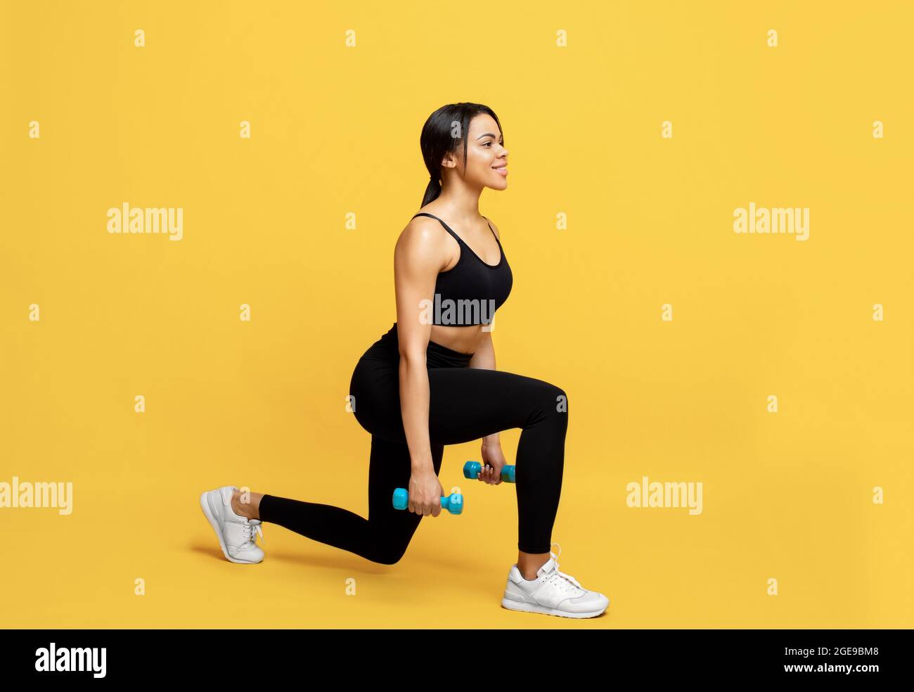 Concept d'entraînement de force. Femme sportive noire faisant de l'exercice de fentes avec des haltères sur fond jaune Banque D'Images