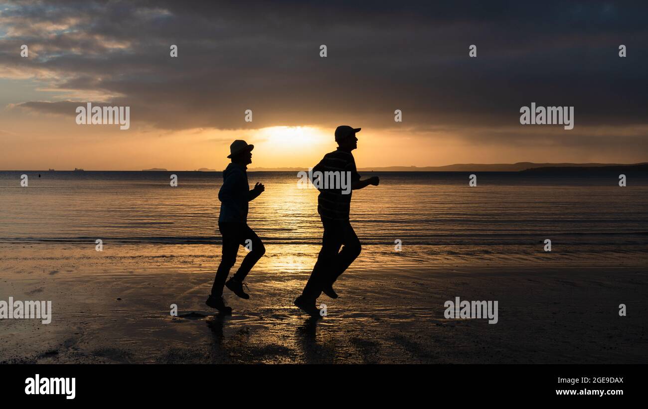 Silhouette de deux personnes qui s'exécutent sur une plage de sable au lever du soleil Banque D'Images