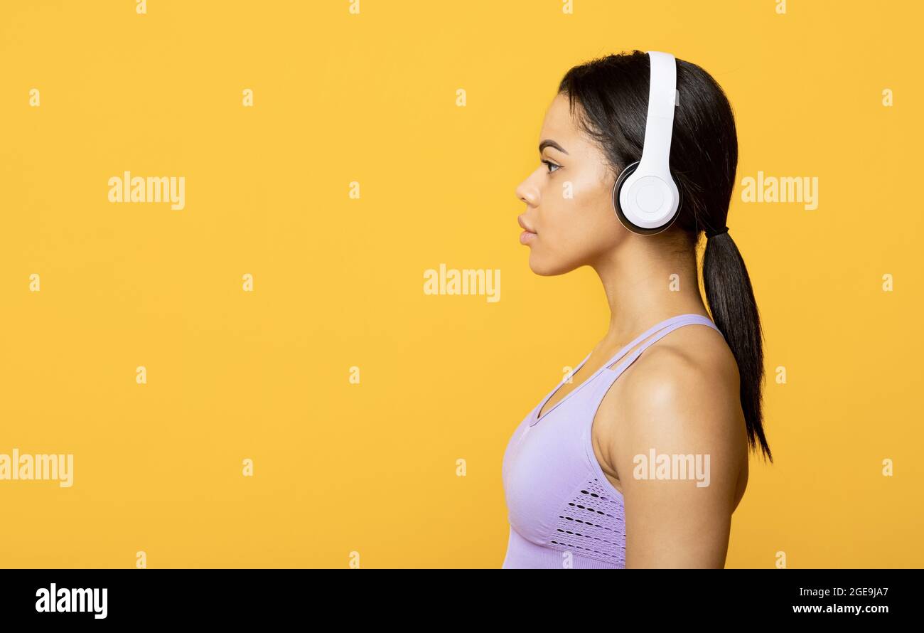 Motivation, musique pour l'entraînement. Jeune femme afro-américaine avec casque regardant l'espace libre, fond jaune Banque D'Images