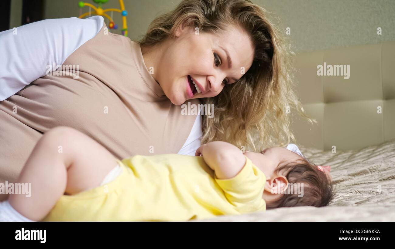 Une mère joyeuse aux cheveux bouclés joue avec bébé au lit Banque D'Images