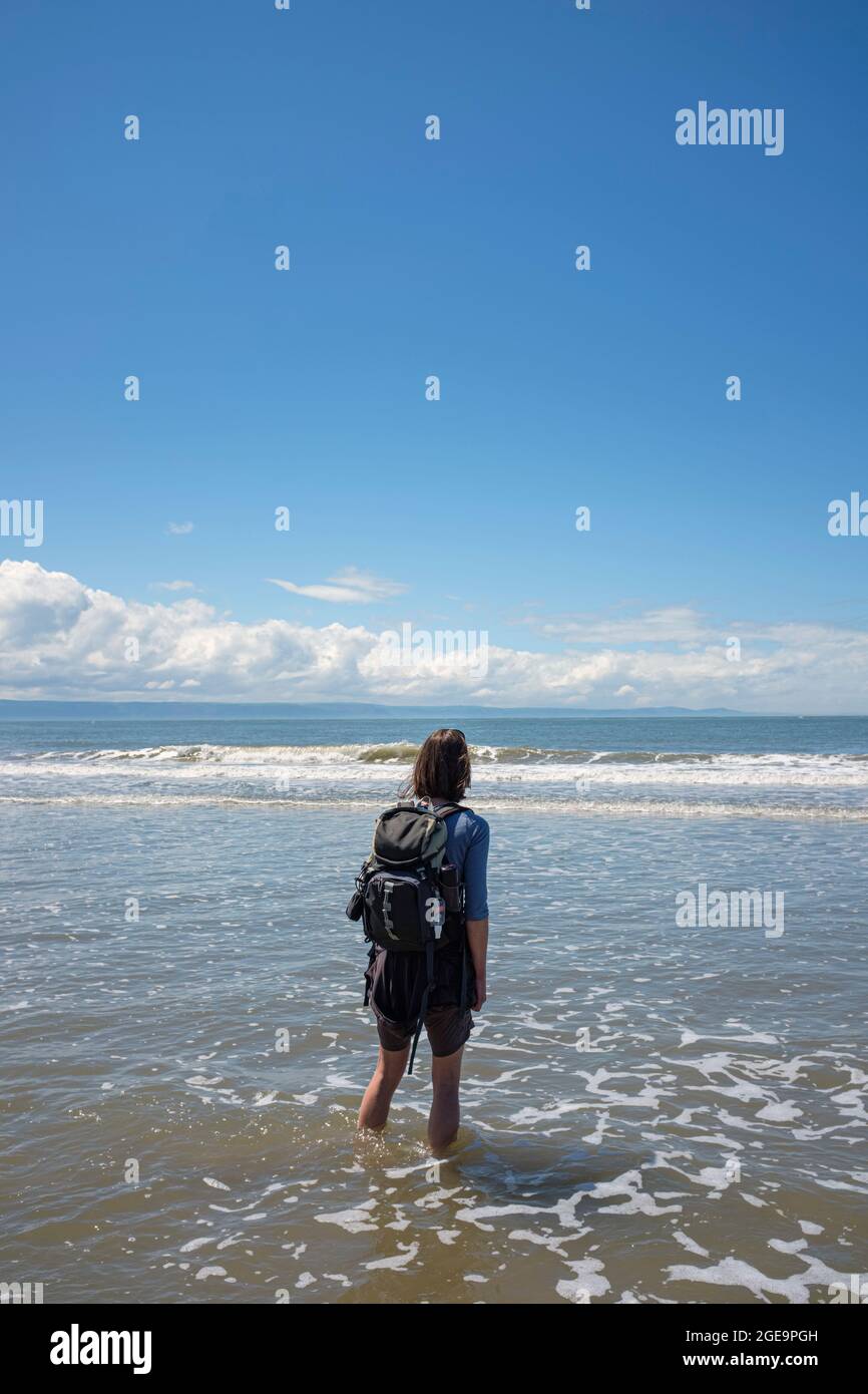 Femme marchant dans des vagues peu profondes sur une plage de sable. Banque D'Images