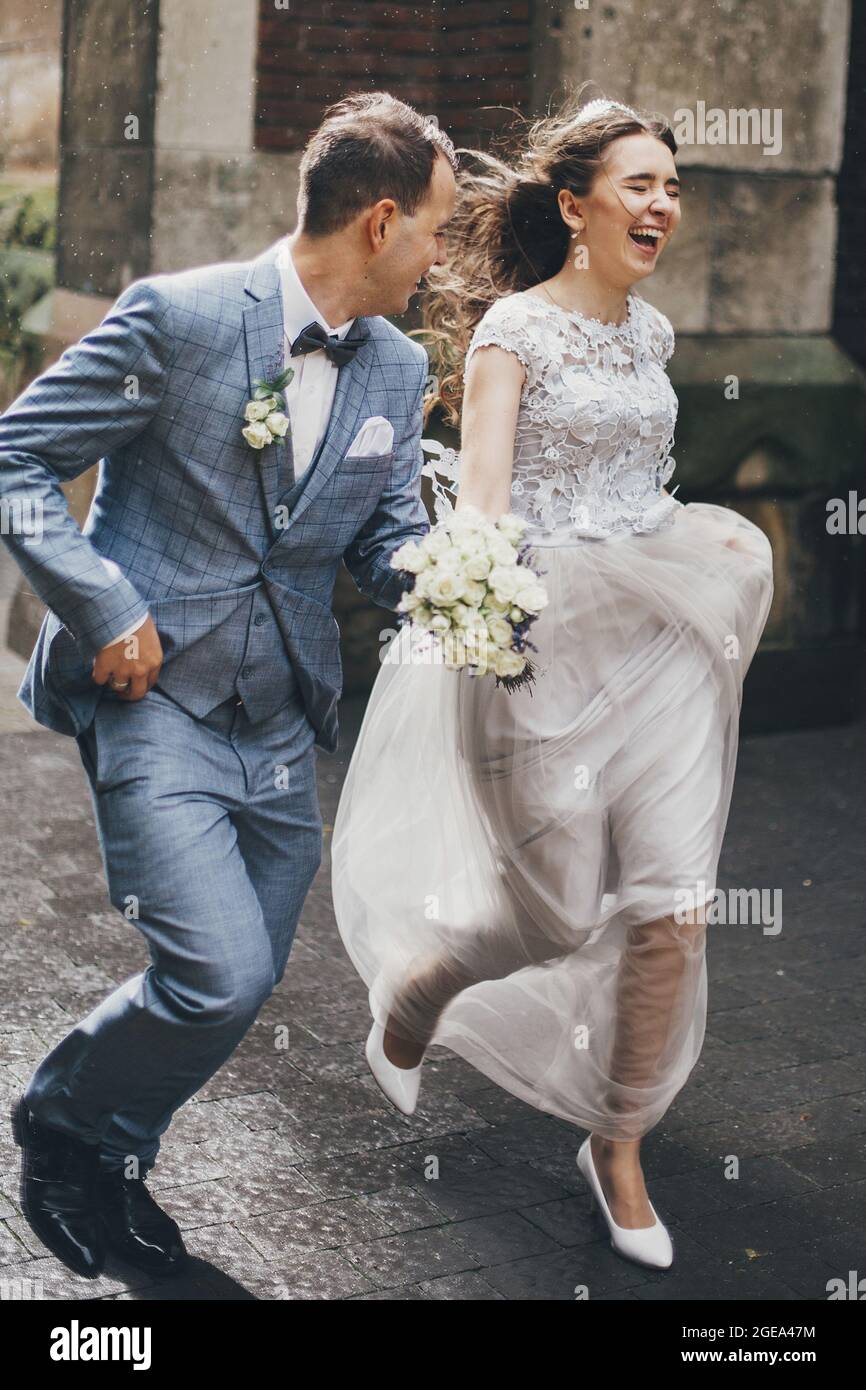 Élégante mariée heureuse et marié courant sur fond de vieille église dans la rue des pluies. Mariage provençal. Beau couple de mariage émotionnel souriant et ha Banque D'Images