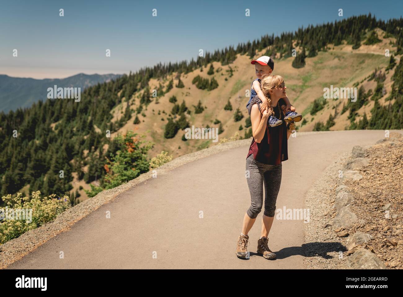 Mère transportant un jeune fils sur les épaules pendant qu'ils font la randonnée sur Hurricane Hill dans le parc national olympique. Banque D'Images