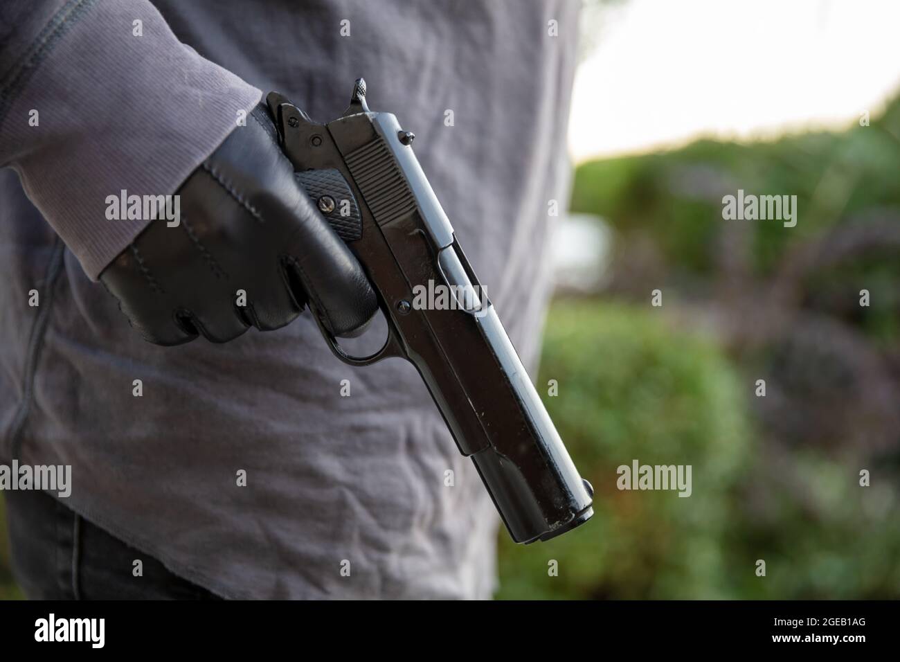 Homme armé en mouvement, tenant un pistolet dans sa main gantée, flou de fond de nature extérieure. Concept de menace, de violence et de danger Banque D'Images