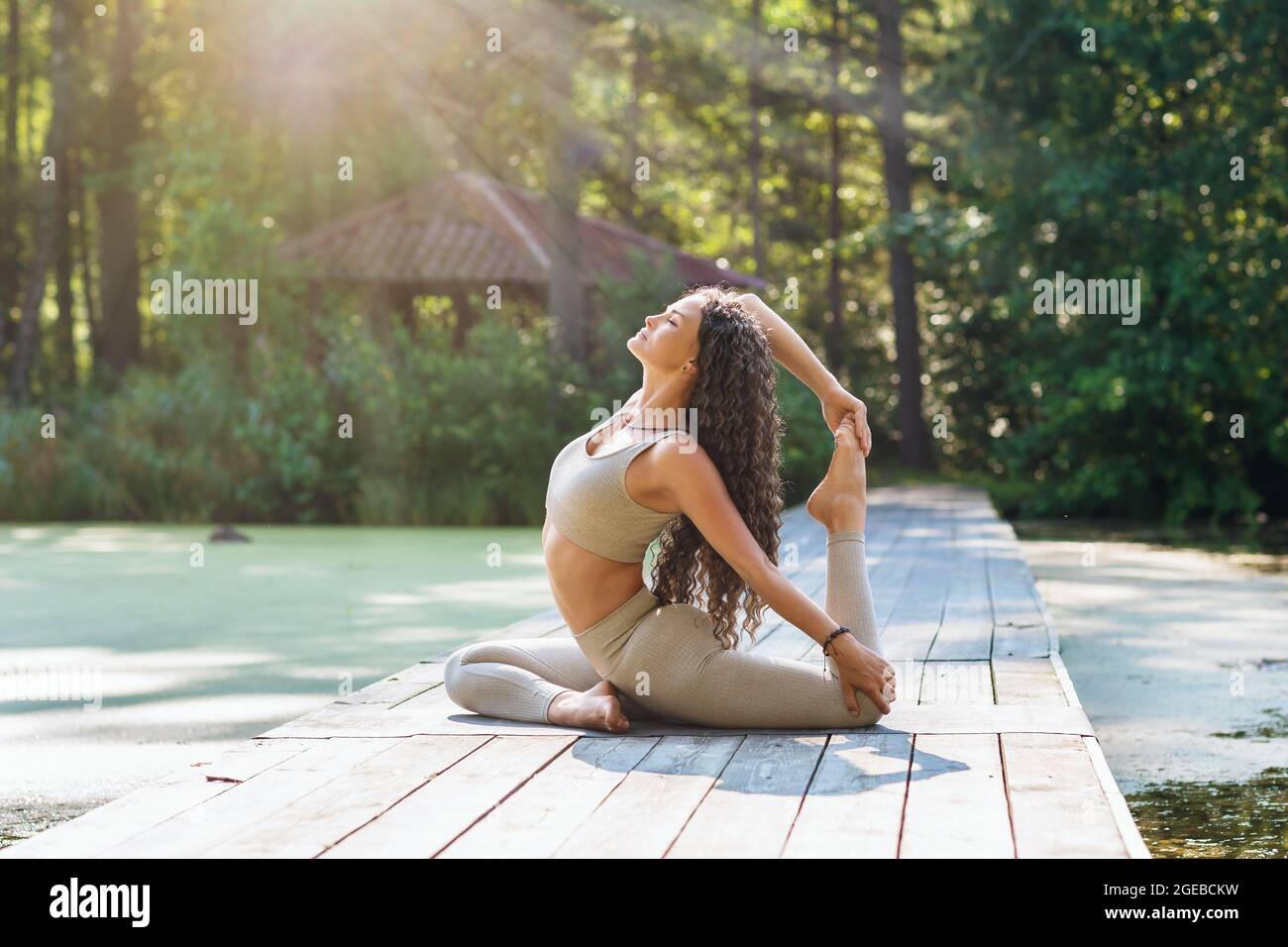 Femme en leggings et haut court, pratiquant le yoga, assis sur un tapis dans le parc, faisant l'exercice eka pada rajakapotasana, posture dove Banque D'Images