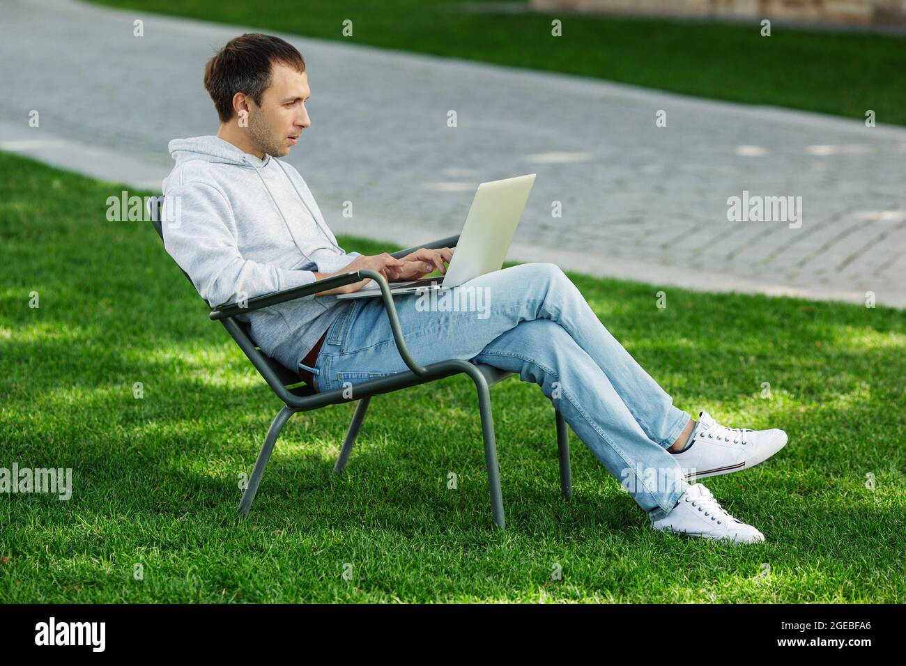 Blogueur homme travaille sur ordinateur portable dans le parc public, traite la vidéo pour le contenu des médias sociaux, assis dans la chaise Banque D'Images