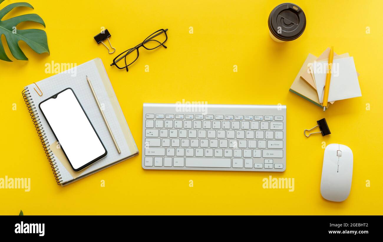 Bureau table bureau avec ordinateur clavier lunettes, smartphone souris bureau fournitures plantes café tasse. Espace de travail plat sur fond jaune coloré Banque D'Images