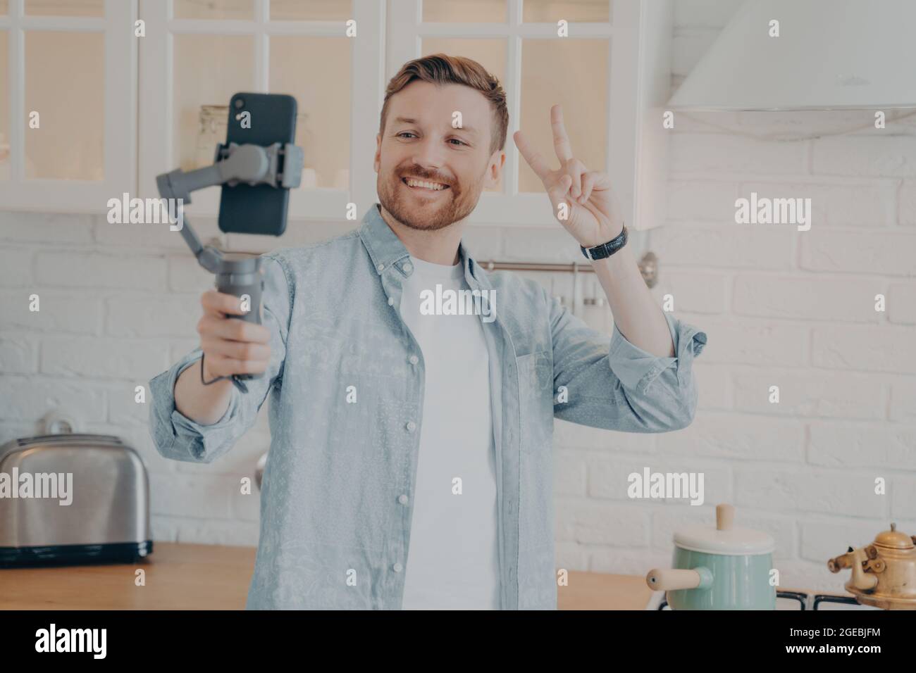 Beau jeune homme brunete souriant avec un chaume qui fait du selfie dans la cuisine Banque D'Images