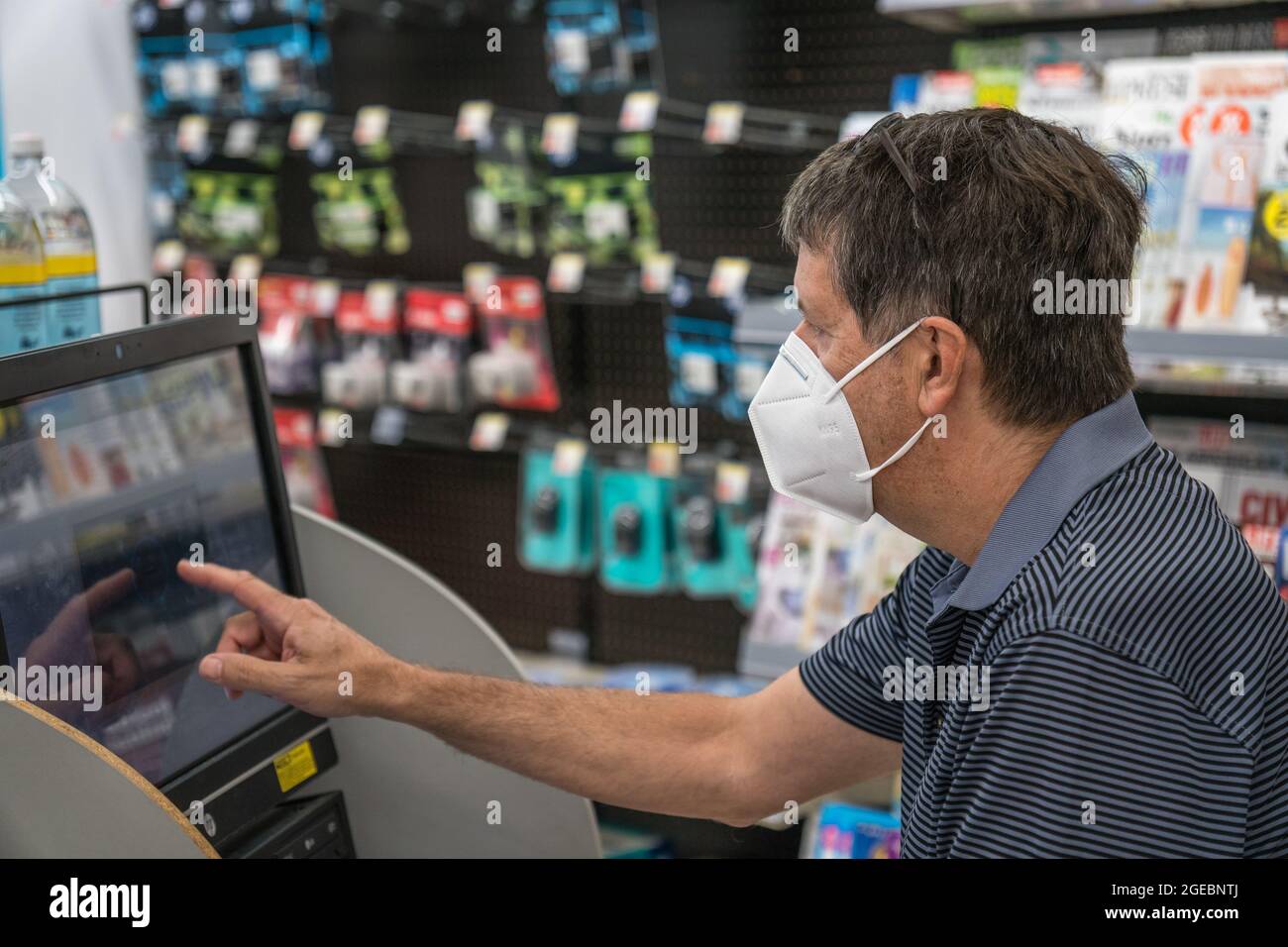 Homme d'âge moyen utilisant un terminal informatique dans un magasin de détail portant un masque KN95 pendant l'ère de la pandémie Covid-19. Banque D'Images