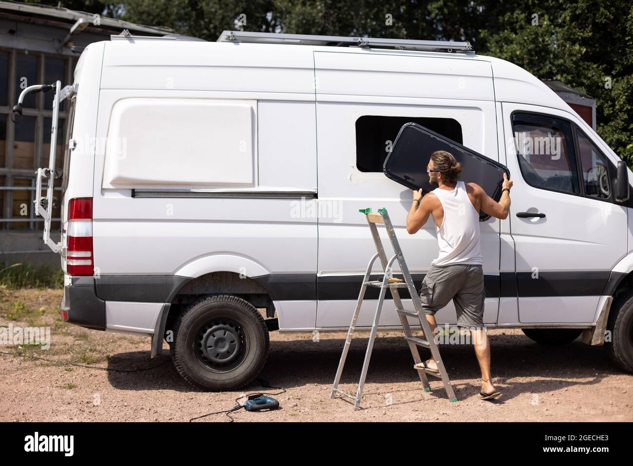 Conversion d'une fourgonnette de camping - un homme installe une vitre latérale Banque D'Images