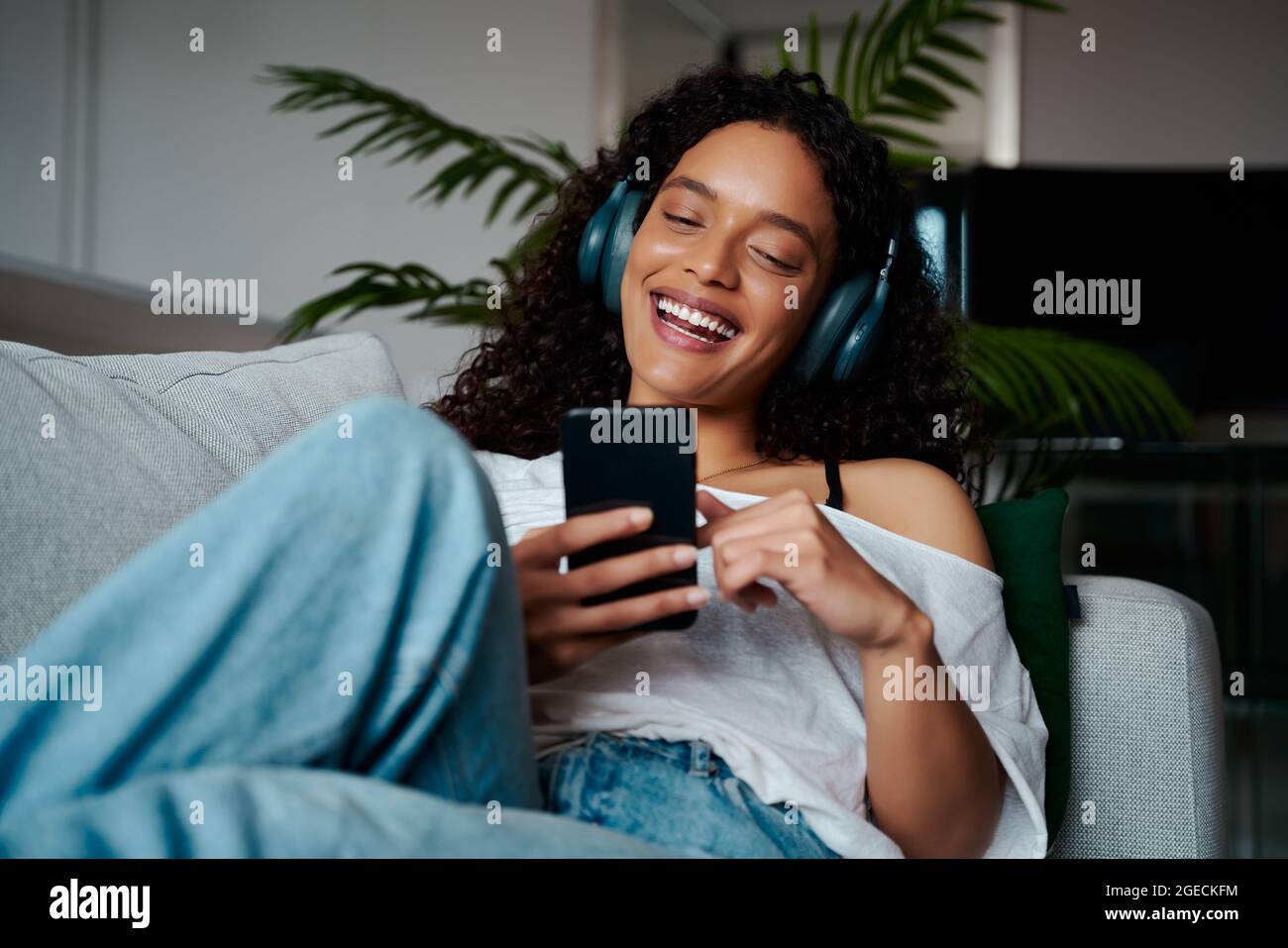 Course mixte femelle adolescence se détendre sur le canapé texting sur un appareil cellulaire Banque D'Images