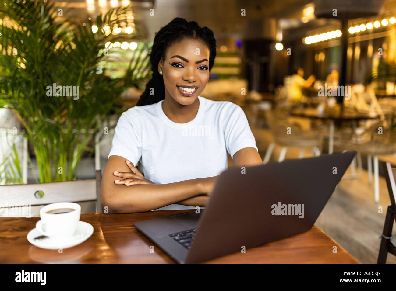 Portrait d'une jeune femme africaine charmante blogueuse, dactylographiant un nouveau poste stimulant pendant le déjeuner dans un café, avec ordinateur portable et smartphone avec copie s. Banque D'Images