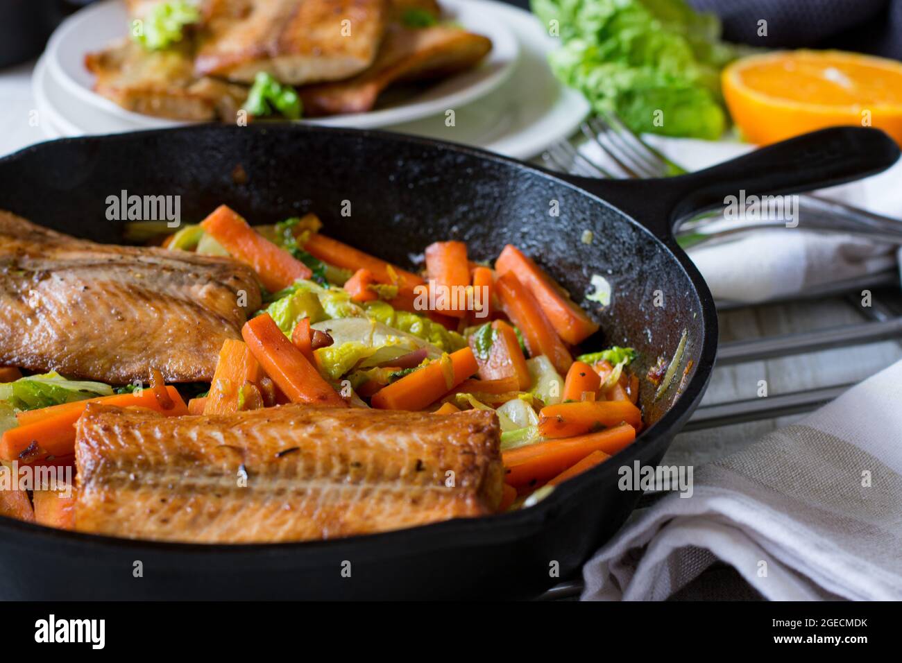 Filet de saumon poêlé avec chou et carottes servi chaud dans une poêle en fonte sur fond de table de cuisine Banque D'Images