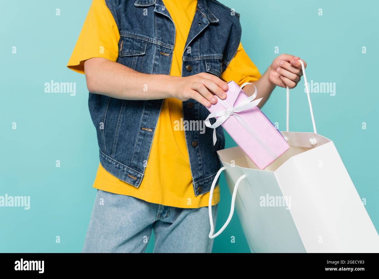 Vue rognée de l'homme mettant boîte cadeau dans un sac de shopping isolé sur bleu Banque D'Images