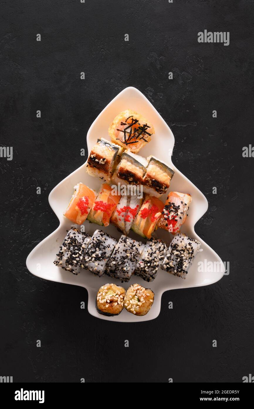 Sushi servi dans l'assiette comme arbre de Noël avec décoration de fête sur fond noir. Vue de dessus. Banque D'Images