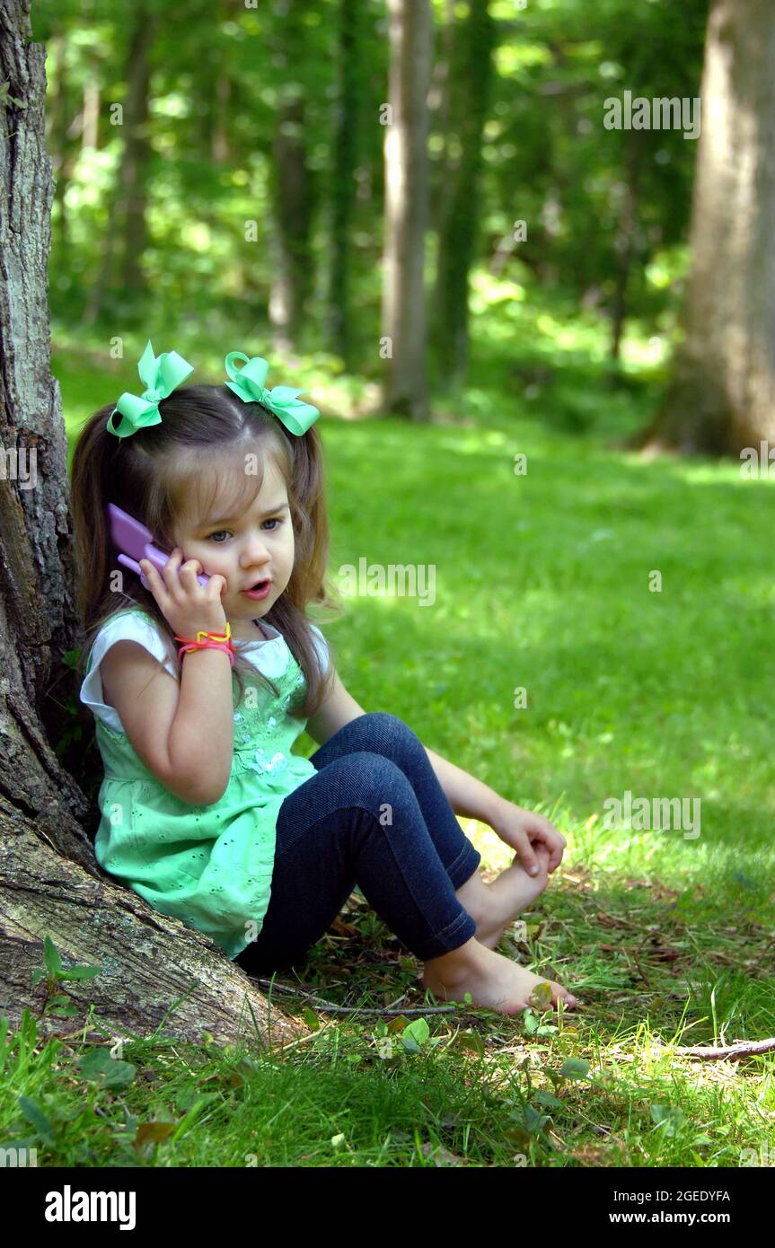 Une petite fille s'immerge dans le jeu de rôle, comme elle parle à son ami imaginaire sur son téléphone de jeu. Elle a des queues de porc et des coiffures vertes. Banque D'Images
