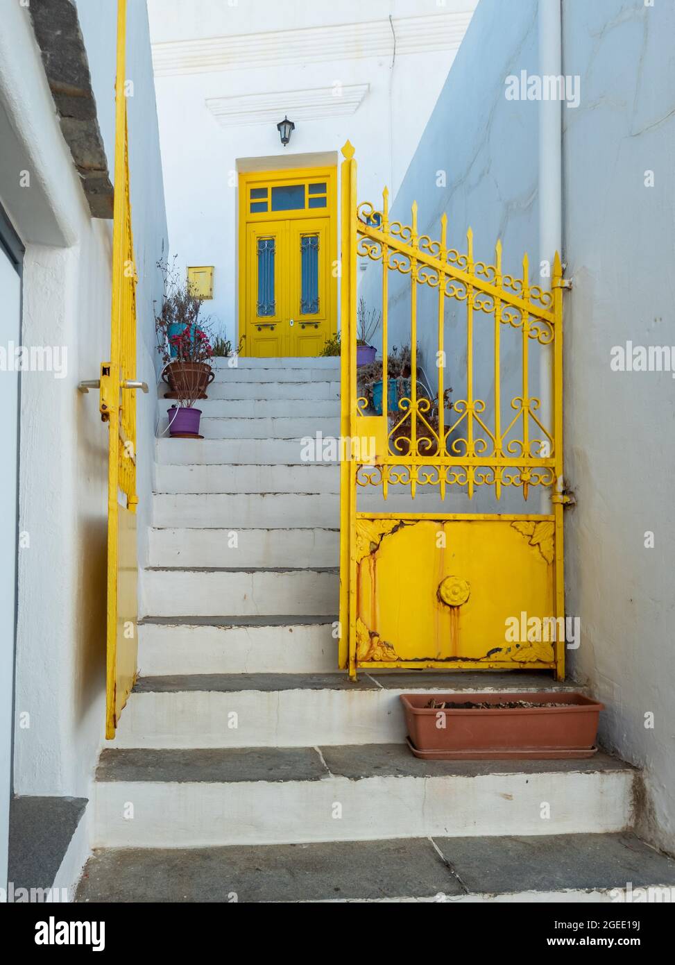 Du métal jaune rouillé porte ouverte à la même couleur portes fermées plantes dans des pots sur des stonestairs vides. Maison traditionnelle blanchie à la chaux sur l'île de Sifnos, Apollo Banque D'Images