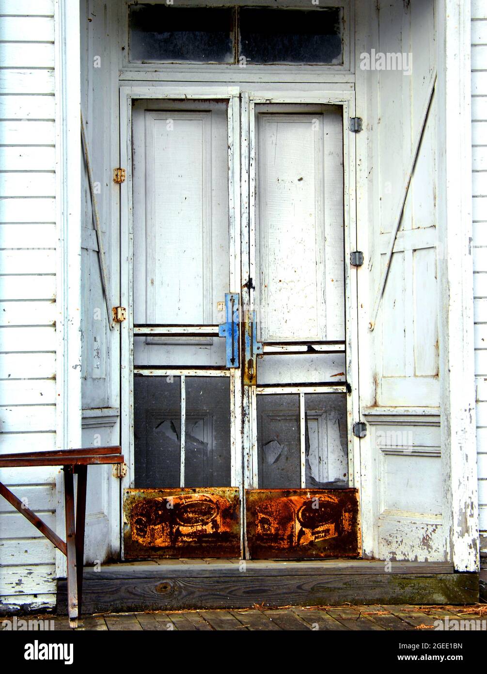 Vieux bois, magasin de pays a des portes doubles avec des protecteurs d'écran et la publicité rouillée au fond. Le magasin est blanc avec l'ancien banc en bois. Banque D'Images