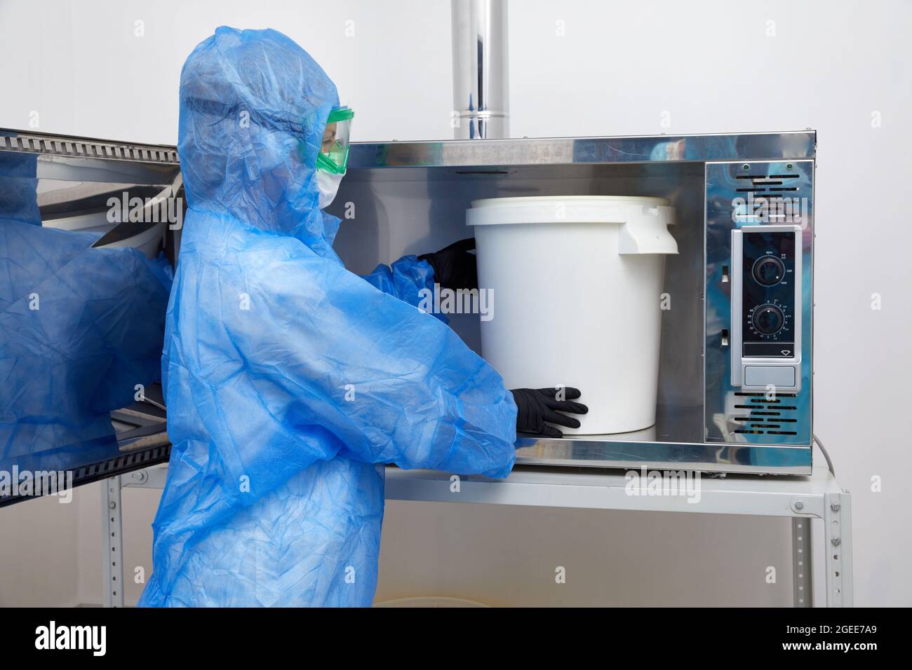 Technologue portant un vêtement de protection EPI, un masque, des gants et travaillant avec un grand seau en plastique dans un laboratoire de recherche Banque D'Images