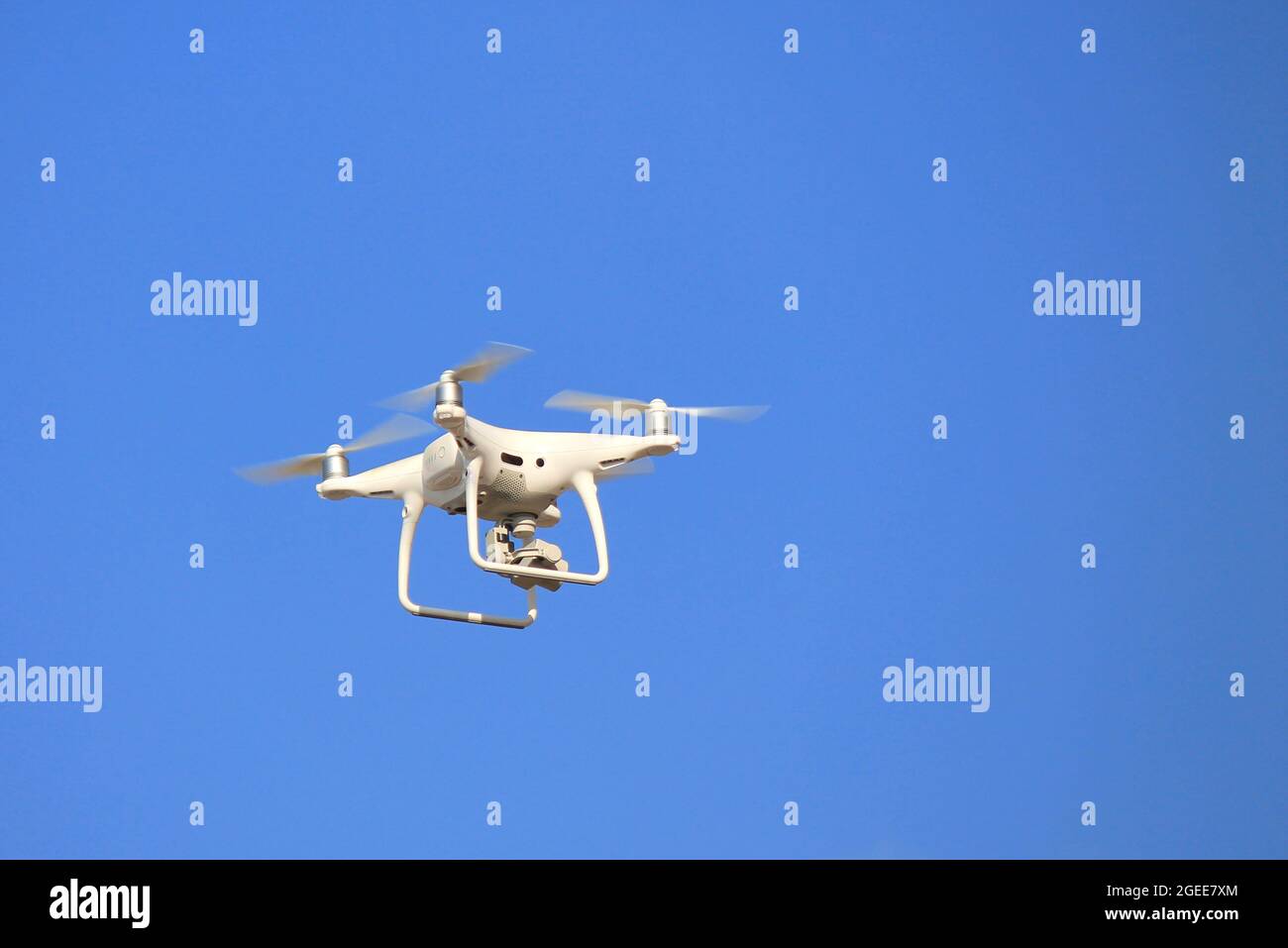 Drone blanc, avec un appareil photo vole contre un ciel bleu sans nuages. Quadrocopter, véhicule aérien sans pilote en vol Banque D'Images