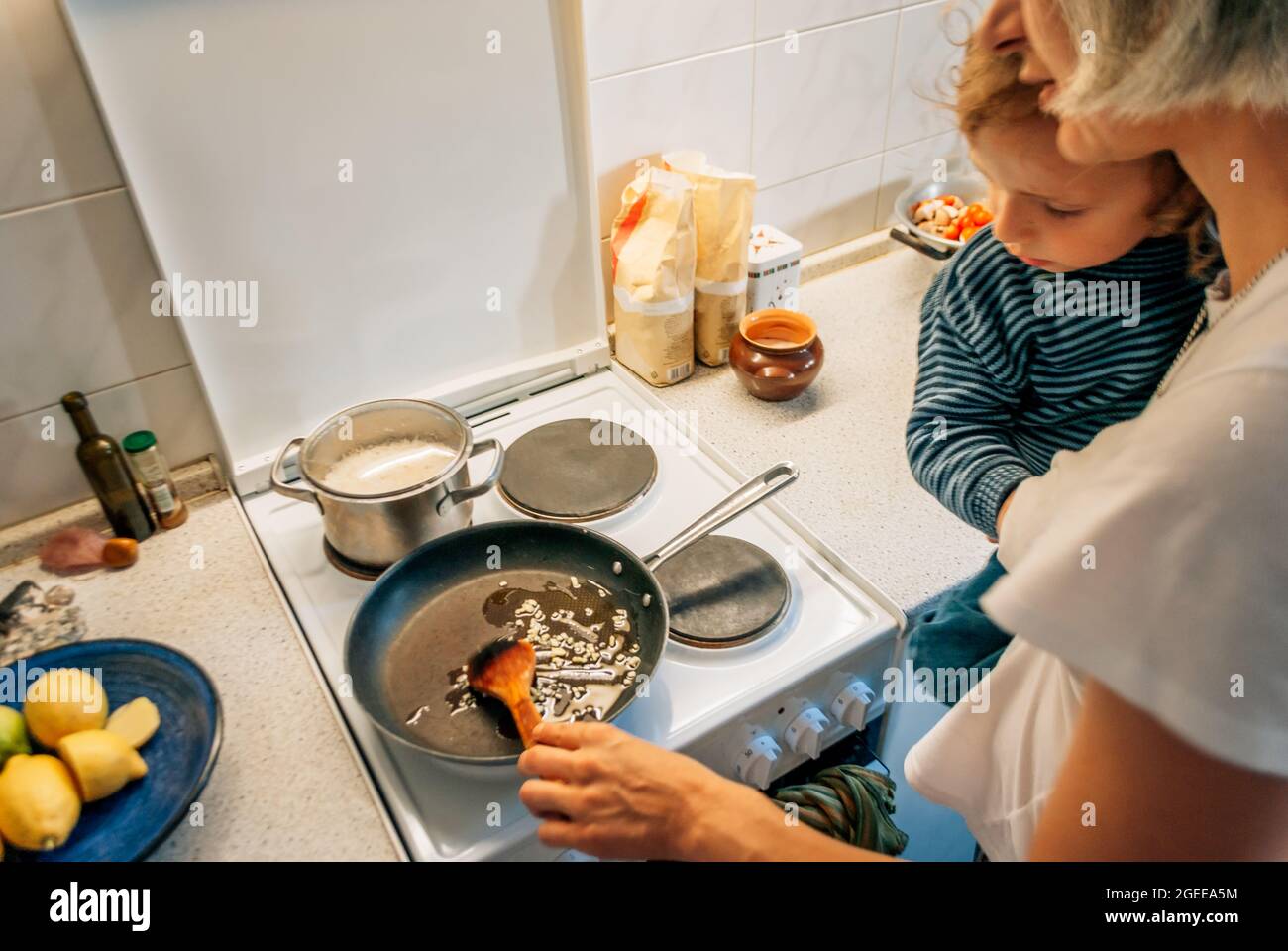 Une femme cuisine dîner à la maison avec un enfant dans ses bras Banque D'Images