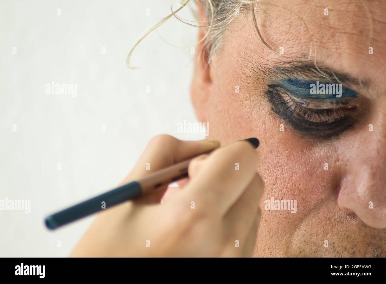 main d'une fille peignant les yeux d'un homme sérieux et mûr avec cosmétique sur fond blanc Banque D'Images