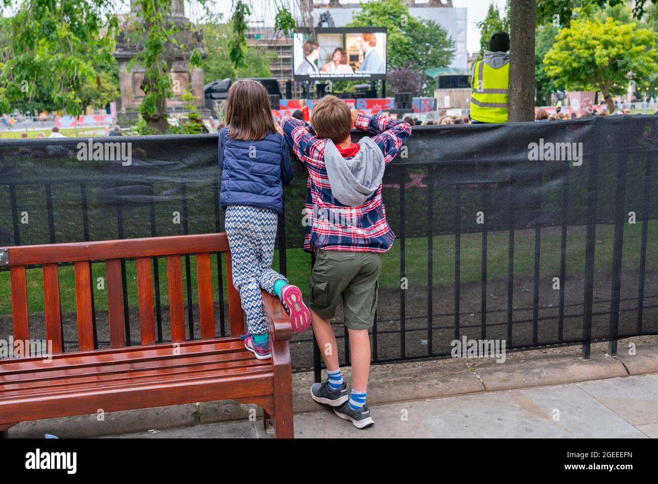 Édimbourg, Écosse, Royaume-Uni. 19 août 2021. Le public regarde une projection en plein air du film culte Ferris Bueller’s Day Off au film Fest dans le cinéma en plein air de la ville, sur la place St Andrew. Il s'agit de l'un des événements qui se déroulent pendant le Festival international du film d'Édimbourg dans la ville. Photo : les jeunes amateurs de cinéma regardent la projection depuis la clôture. Iain Masterton/Alamy Live News. Banque D'Images