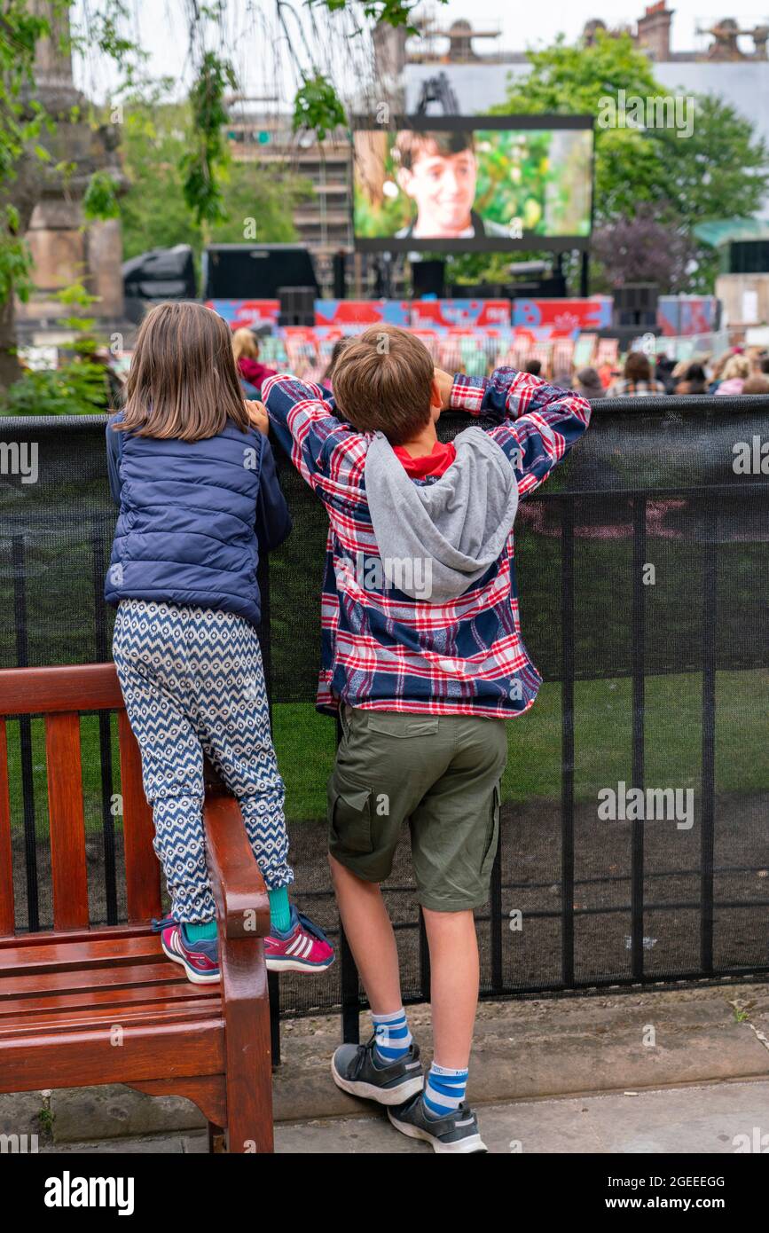 Édimbourg, Écosse, Royaume-Uni. 19 août 2021. Le public regarde une projection en plein air du film culte Ferris Bueller’s Day Off au film Fest dans le cinéma en plein air de la ville, sur la place St Andrew. Il s'agit de l'un des événements qui se déroulent pendant le Festival international du film d'Édimbourg dans la ville. Photo : les jeunes amateurs de cinéma regardent la projection depuis la clôture. Iain Masterton/Alamy Live News. Banque D'Images