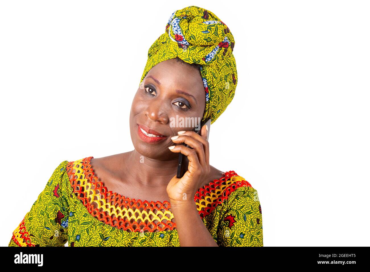 Belle femme adulte africaine portant un chiffon et une écharpe verte sourit au téléphone Banque D'Images