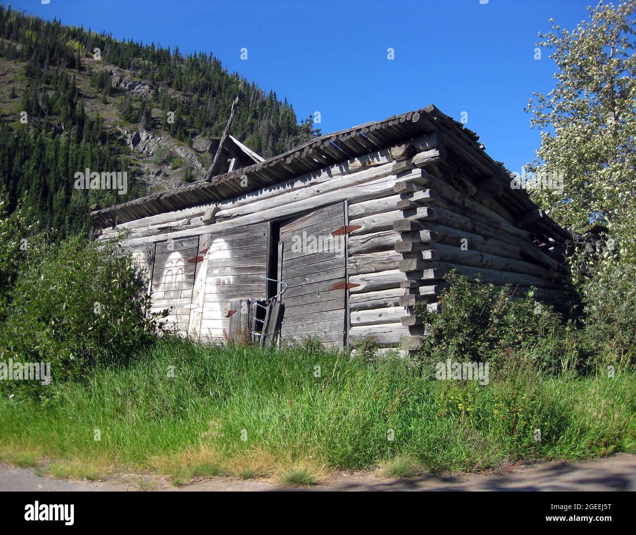 Le vieux hangar en rondins a été peint avec un fantôme sur la porte pour effrayer les visiteurs indésirables. Les montagnes rustiques s'élèvent en arrière-plan. Banque D'Images