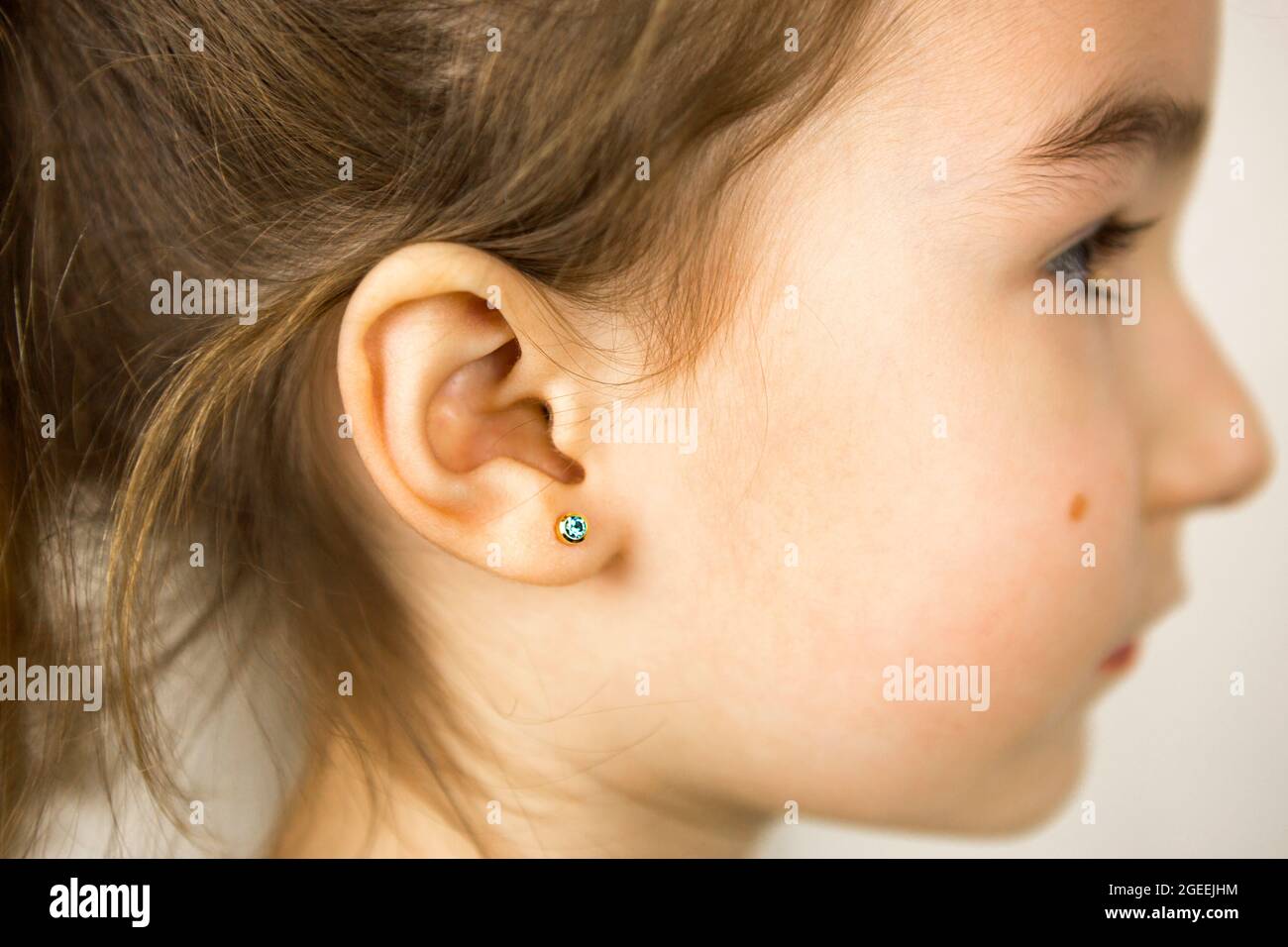 Perçage d'oreilles chez un enfant - une fille montre un anneau auriculaire  dans son oreille fait d'un alliage médical. Fond blanc, portrait d'une  fille avec une taupe sur sa joue Photo Stock -