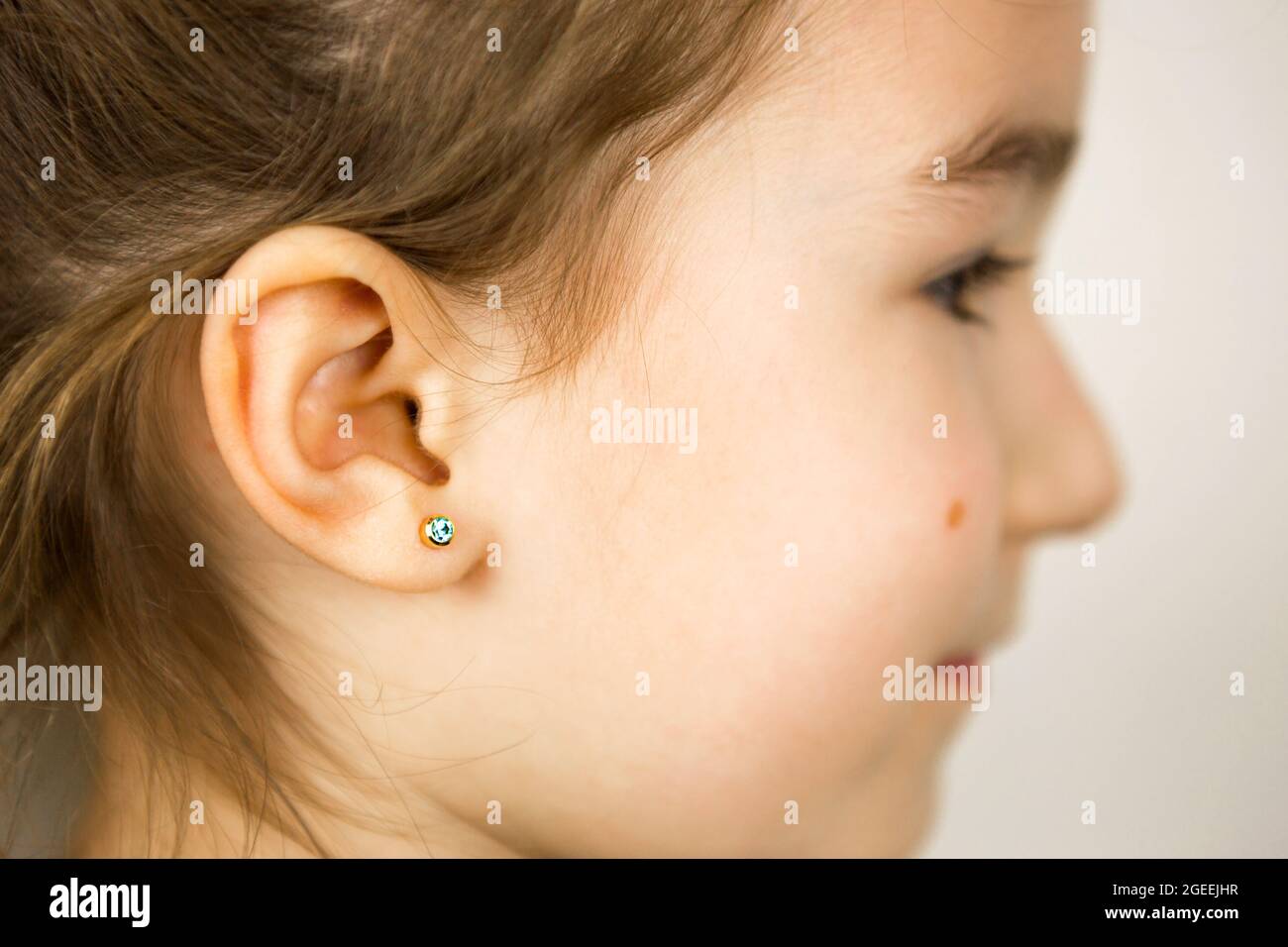 Perçage d'oreilles chez un enfant - une fille montre un anneau auriculaire  dans son oreille fait d'un alliage médical. Fond blanc, portrait d'une fille  avec une taupe sur sa joue Photo Stock -