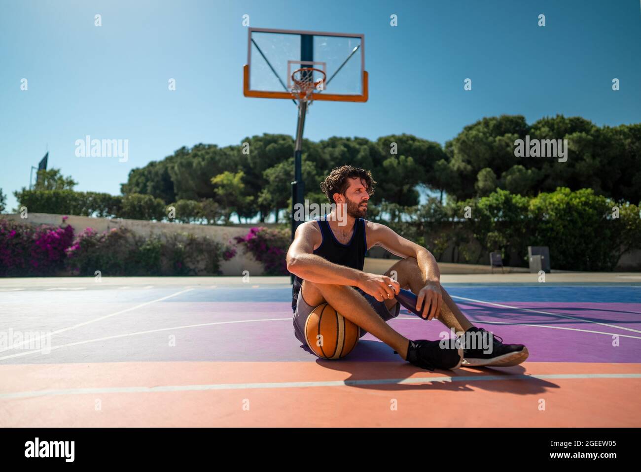 Un joueur de basket-ball de l'homme fatigué est assis sur le sol avec de l'eau après l'entraînement Banque D'Images