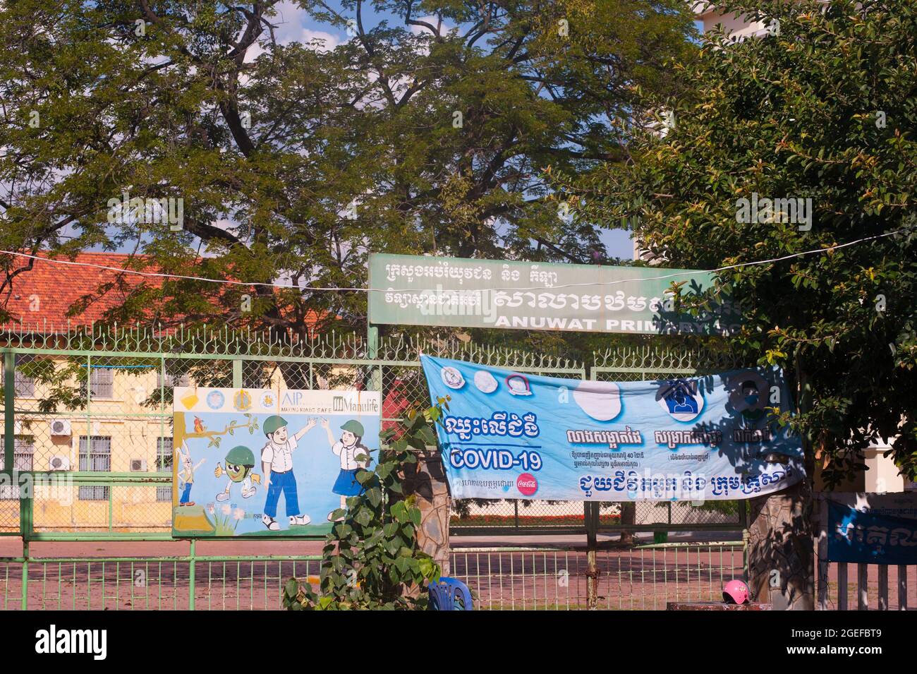 Une école primaire fermée raccroche une bannière bilingue COVID - 19 à côté d'un panneau peint à la main à l'entrée de l'école. Les écoles ont été fermées à Phnom Penh pendant plus de 5 mois en raison de la pandémie du coronavirus. Phnom Penh, Cambodge. 18 août 2021. © Kraig Lieb Banque D'Images