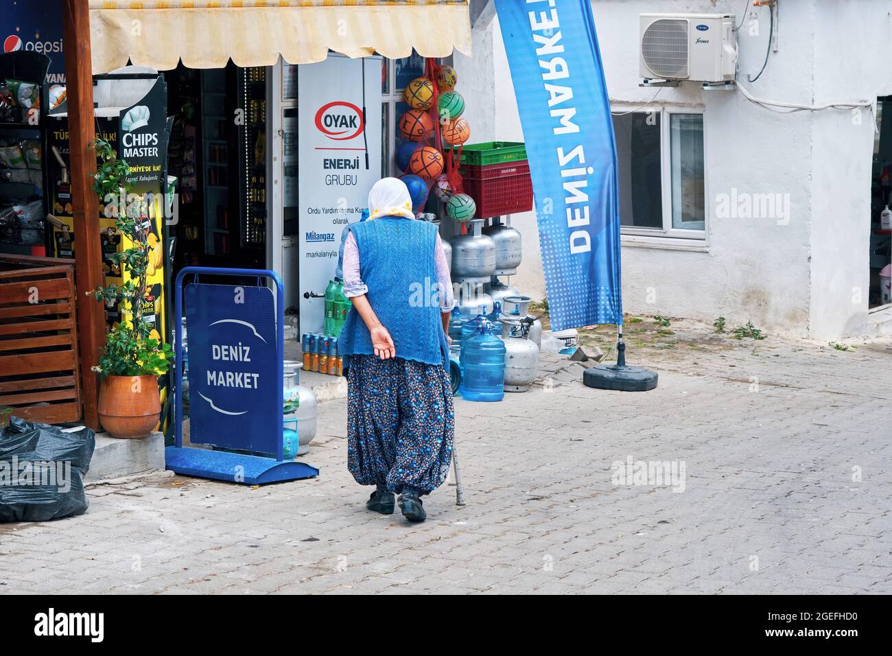 Urla, Izmir, Turquie - juin 2021 : femme âgée marchant avec sa canne vers une épicerie rurale dans le village de Bademler, Urla, Izmir, Turquie. Banque D'Images