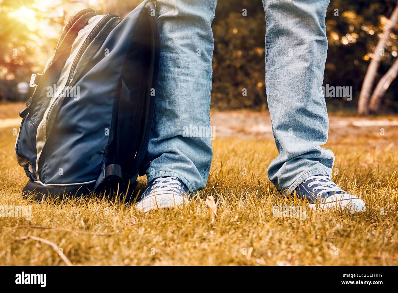 Pied et jambes pour jeune adolescent avec baskets, jeans et sac à dos sur gazon d'automne. Concept de retour à l'école. Banque D'Images