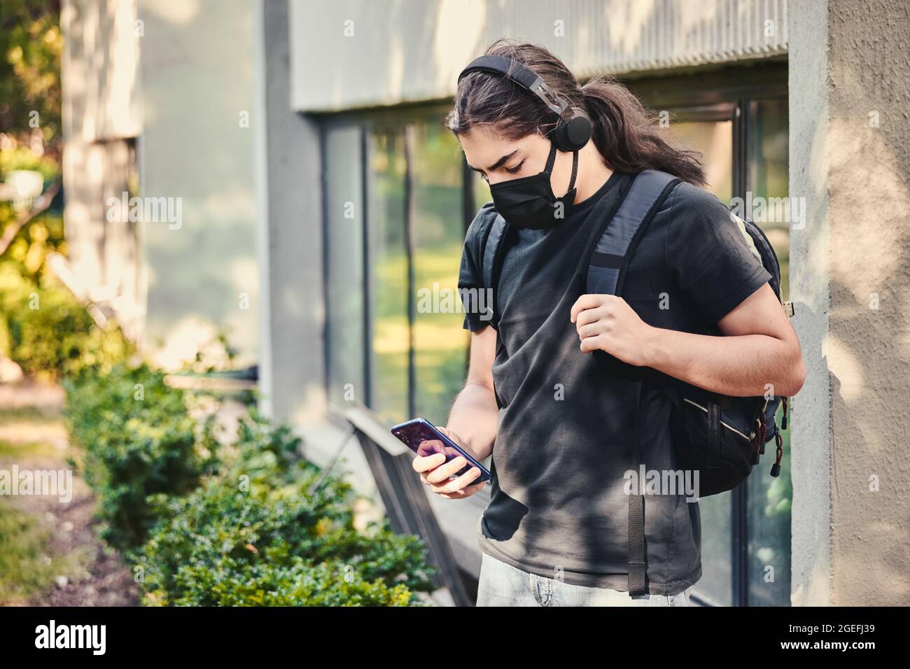 Jeune adolescent lycée garçon avec masque médical, casque et sac à dos,  textant avec son smartphone mobile au jardin de l'école Photo Stock - Alamy