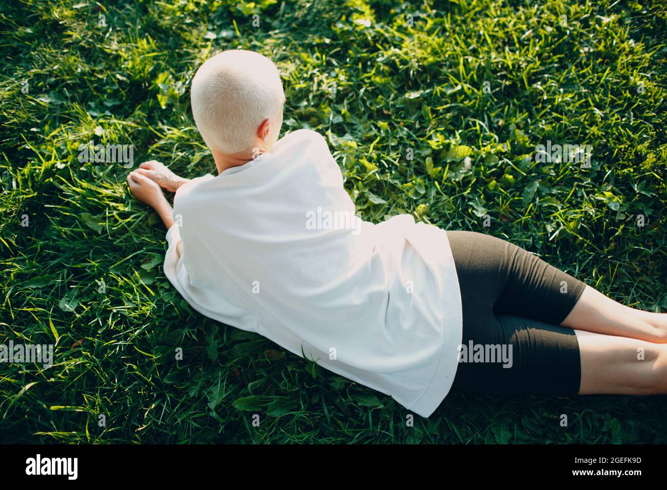 Portrait d'une jeune femme européenne à poil court souriant, posée à l'estomac, herbe verte, prairie, parc d'été, vue aérienne supérieure. Belle fillette blonde heureuse en plein air. Banque D'Images