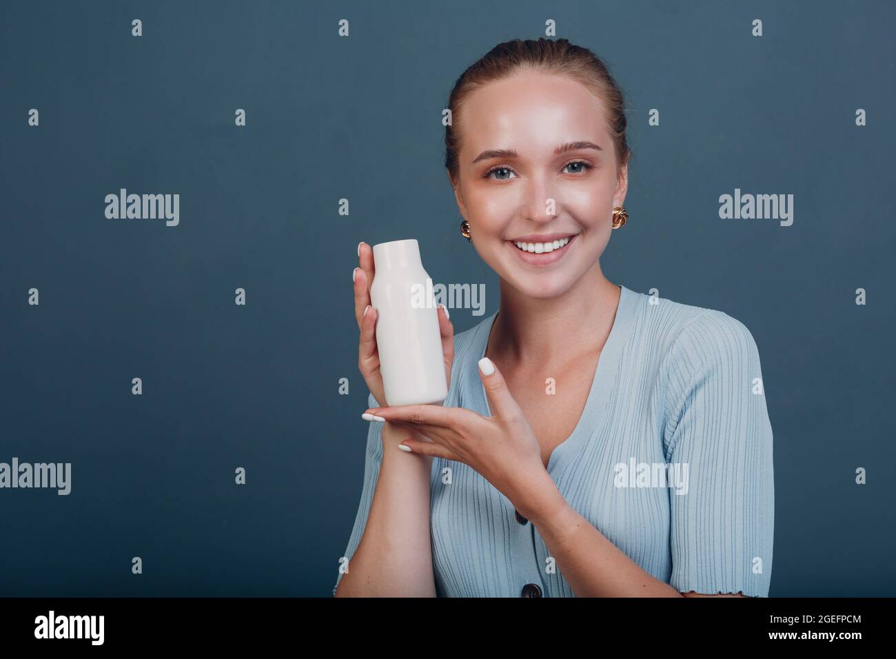 Jolie jeune femme européenne tient blanc modèle de bouteille vide espace vide. Shampooing ou cosmétiques Banque D'Images