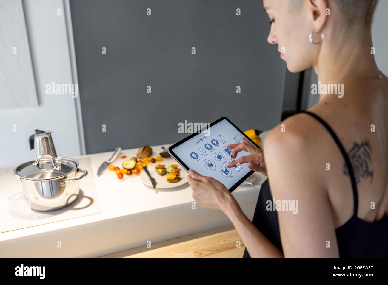 Une femme contrôle les appareils de cuisine intelligents avec un appareil mobile Banque D'Images