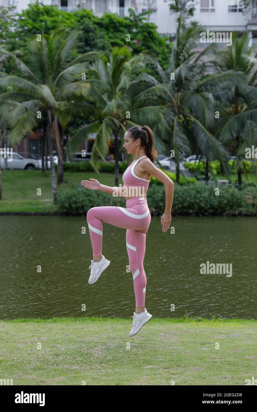 Vue latérale d'une jeune femme sportive en rose sport et en blanc Sneakers sautant. Exercice dans le parc. Photo de haute qualité Banque D'Images